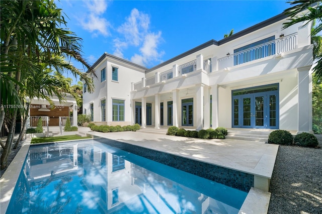 rear view of house with an outdoor pool, a balcony, french doors, a patio area, and stucco siding