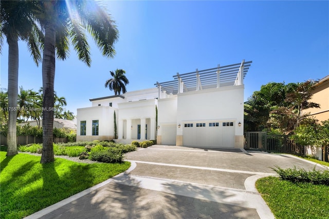 art deco inspired home with decorative driveway, stucco siding, an attached garage, fence, and a front lawn