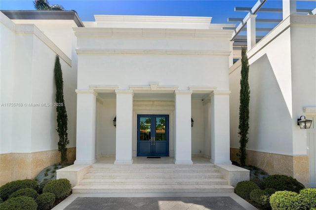 entrance to property featuring a porch, french doors, and stucco siding