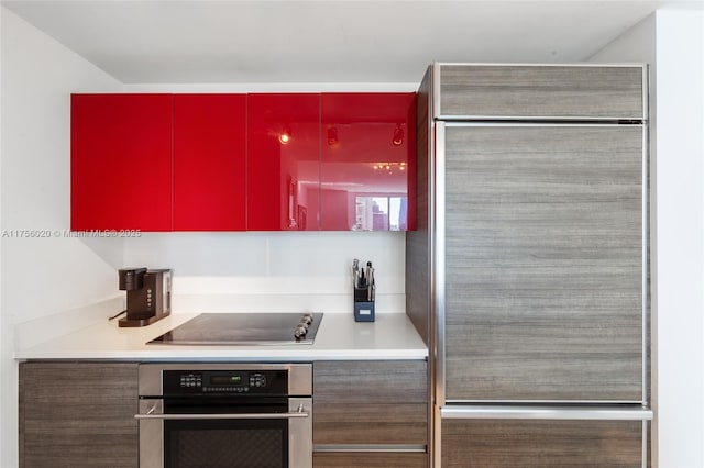 kitchen with red cabinetry, black electric stovetop, built in refrigerator, stainless steel oven, and light countertops