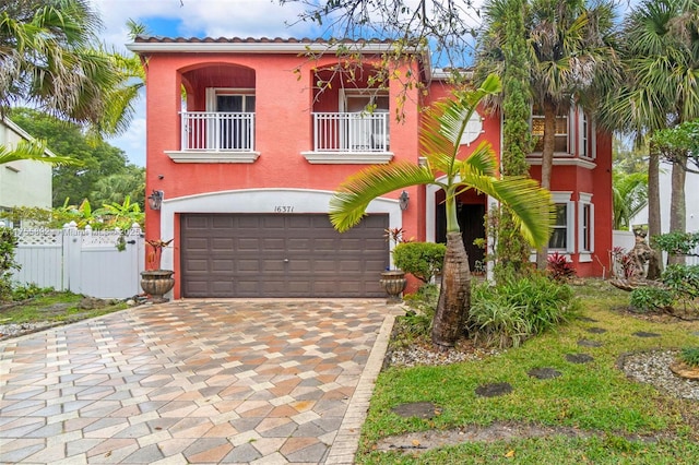 mediterranean / spanish-style house with a garage, a balcony, fence, and stucco siding