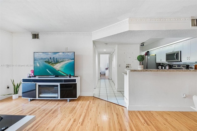 living room featuring baseboards, light wood-style flooring, visible vents, and a textured ceiling