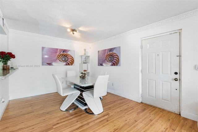 dining room featuring light wood-style floors, crown molding, and baseboards