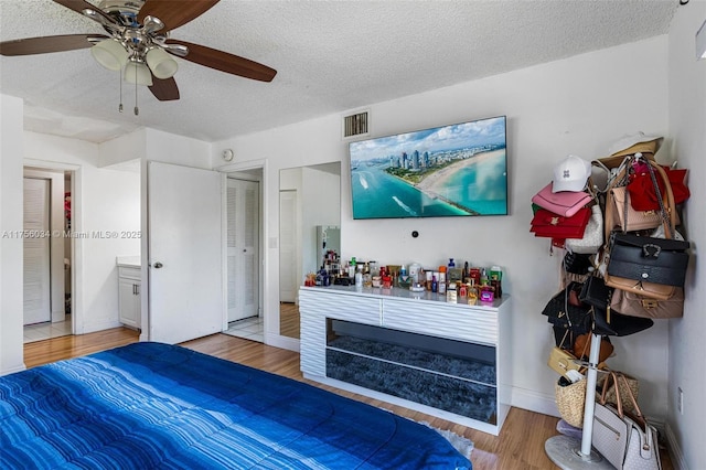 bedroom with a textured ceiling, wood finished floors, visible vents, baseboards, and a ceiling fan