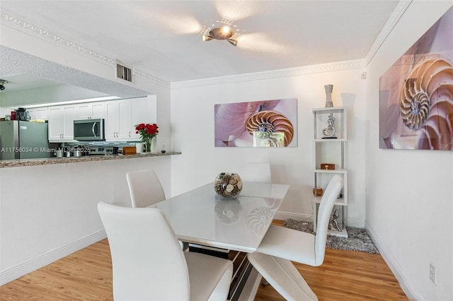 dining area featuring ornamental molding, visible vents, light wood-style flooring, and baseboards