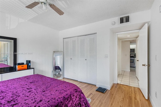 bedroom featuring a textured ceiling, wood finished floors, visible vents, baseboards, and a closet