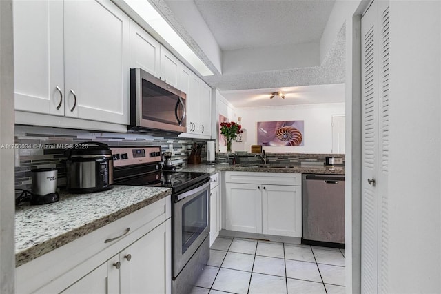 kitchen featuring light tile patterned floors, decorative backsplash, appliances with stainless steel finishes, white cabinets, and a sink