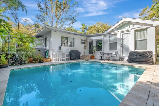 rear view of property featuring an outdoor pool, a patio, and stucco siding