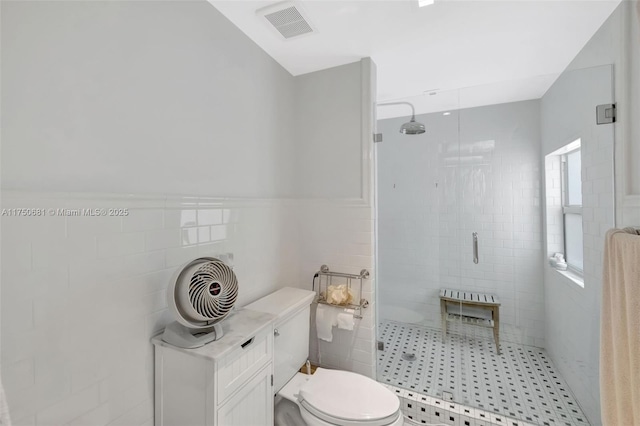 full bathroom with a stall shower, visible vents, wainscoting, toilet, and tile walls