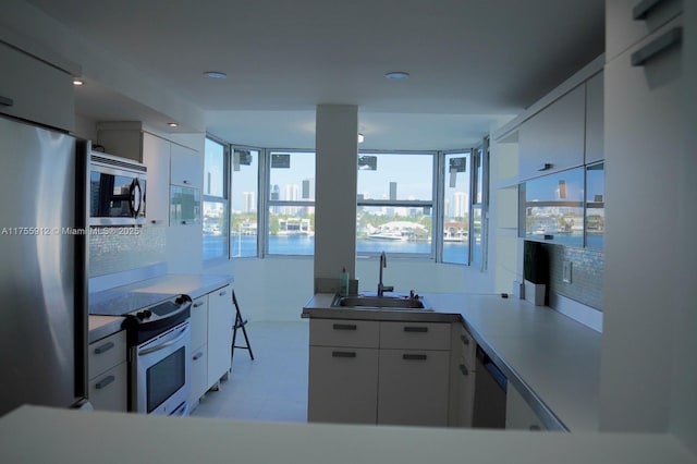 kitchen with white cabinets, appliances with stainless steel finishes, a sink, light countertops, and backsplash