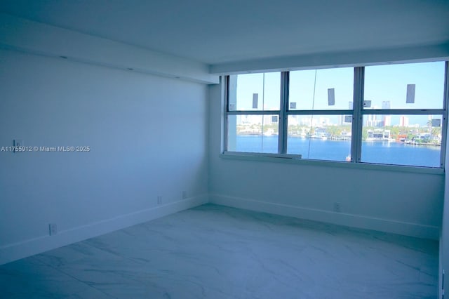 unfurnished room with a healthy amount of sunlight, marble finish floor, and baseboards