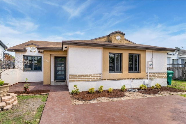 view of front of home featuring brick siding, fence, and stucco siding