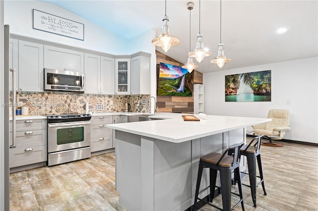 kitchen with a breakfast bar area, lofted ceiling, light countertops, backsplash, and appliances with stainless steel finishes