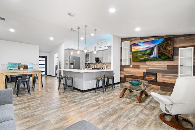 living room featuring lofted ceiling, a glass covered fireplace, visible vents, and wooden walls