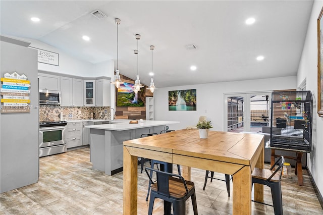 kitchen with lofted ceiling, stainless steel appliances, visible vents, light countertops, and glass insert cabinets