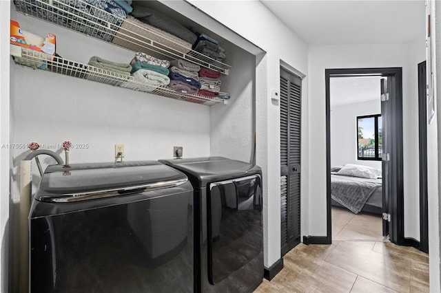 clothes washing area with laundry area, baseboards, washing machine and clothes dryer, and light tile patterned floors