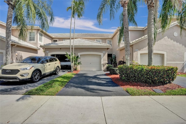 multi unit property featuring a garage, aphalt driveway, a tiled roof, and stucco siding