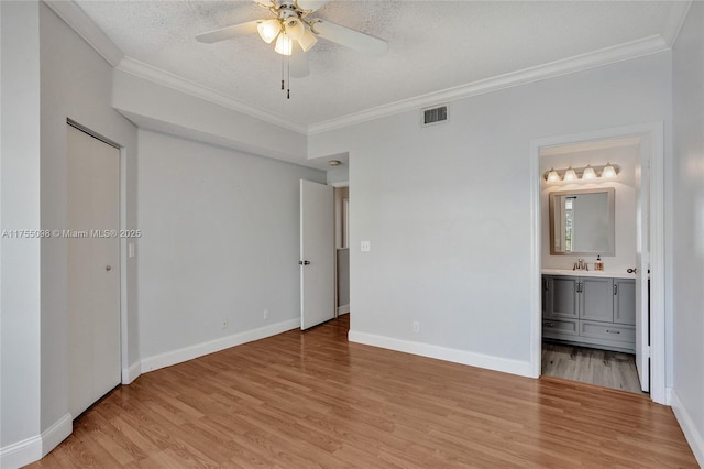 unfurnished bedroom featuring a textured ceiling, a sink, visible vents, light wood finished floors, and crown molding