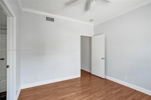 empty room featuring a textured ceiling, ornamental molding, wood finished floors, and visible vents