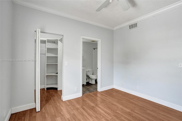 unfurnished bedroom with visible vents, ornamental molding, a closet, light wood finished floors, and a walk in closet