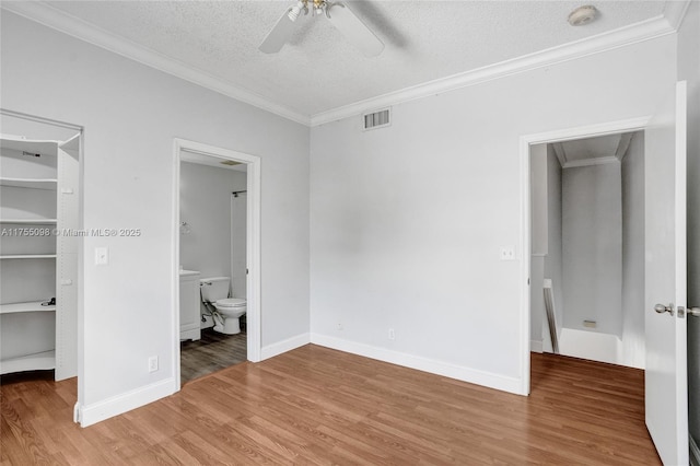 unfurnished bedroom featuring light wood-type flooring, visible vents, crown molding, and a spacious closet