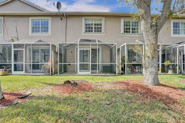 back of house with glass enclosure, a lawn, and stucco siding