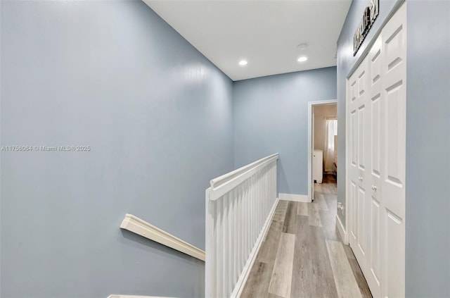 hallway with light wood-type flooring, baseboards, an upstairs landing, and recessed lighting