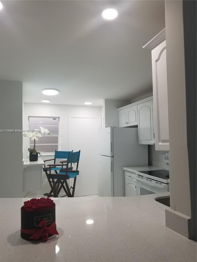 kitchen featuring light stone counters, white appliances, and white cabinets