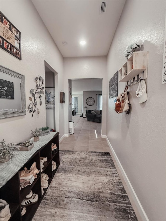 hallway featuring a textured wall, tile patterned flooring, visible vents, and baseboards