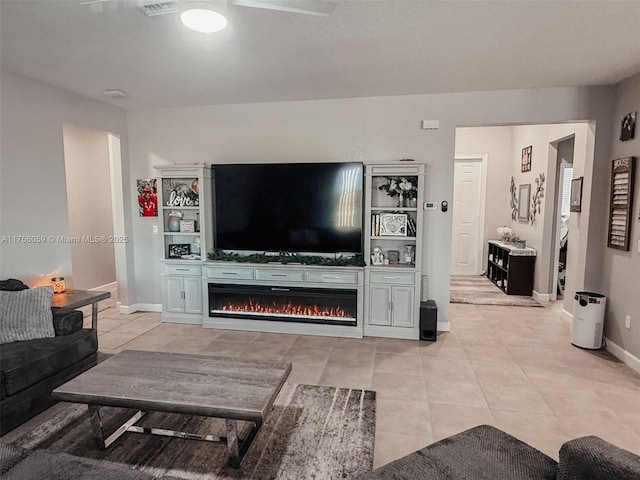 living room featuring a glass covered fireplace, visible vents, baseboards, and light tile patterned floors