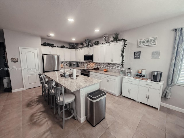 kitchen featuring backsplash, appliances with stainless steel finishes, white cabinetry, a sink, and a kitchen breakfast bar