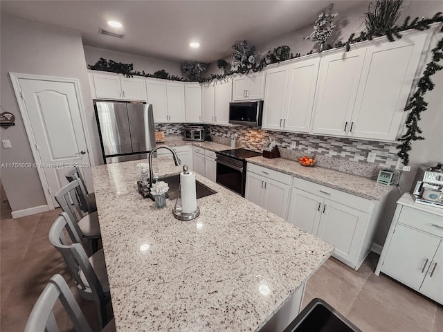 kitchen with visible vents, a sink, a kitchen island with sink, stainless steel appliances, and backsplash