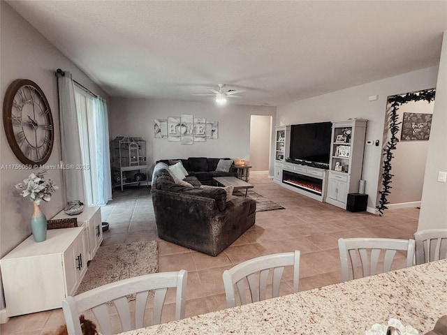 living area featuring light tile patterned flooring, ceiling fan, a textured ceiling, a lit fireplace, and baseboards