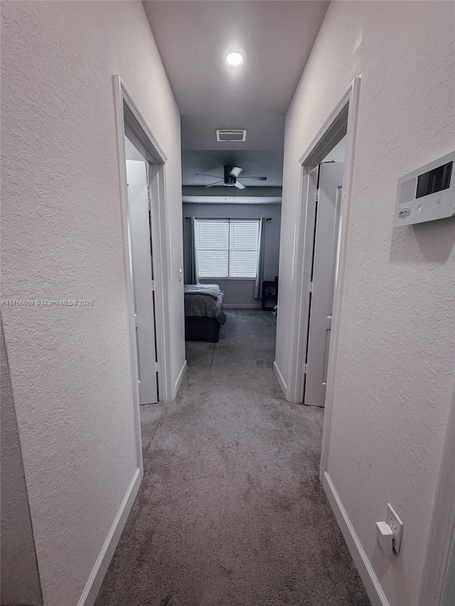 corridor featuring a textured wall, carpet floors, visible vents, and baseboards