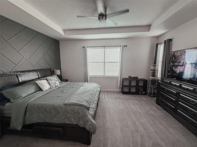 carpeted bedroom featuring a ceiling fan, a raised ceiling, and baseboards