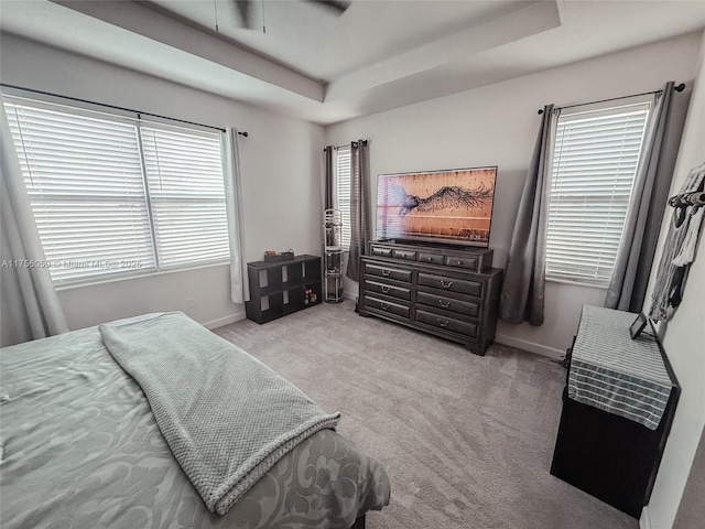 carpeted bedroom with a tray ceiling and baseboards