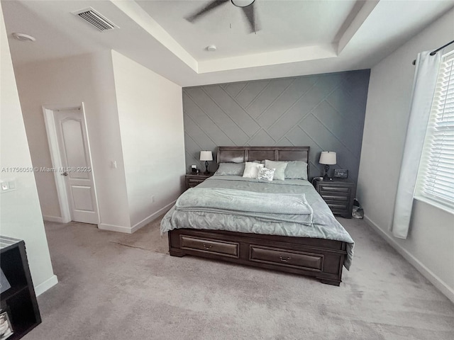 bedroom featuring an accent wall, a tray ceiling, visible vents, and baseboards