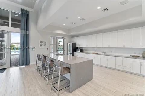 kitchen featuring white cabinetry, freestanding refrigerator, light wood finished floors, a raised ceiling, and a large island with sink