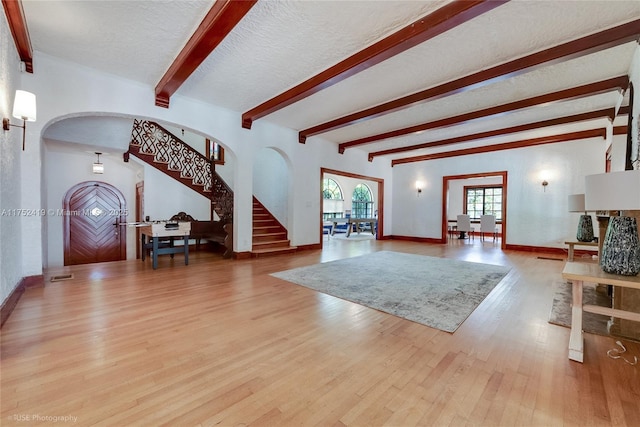 living area with arched walkways, wood finished floors, beamed ceiling, stairs, and a textured ceiling