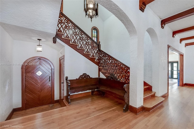 entryway with beamed ceiling, wood finished floors, stairway, arched walkways, and baseboards