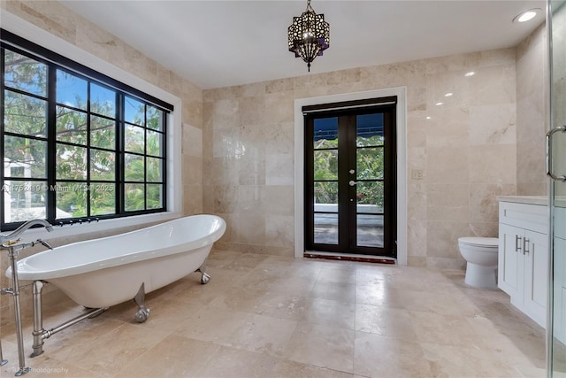 bathroom featuring toilet, a freestanding tub, vanity, and tile walls