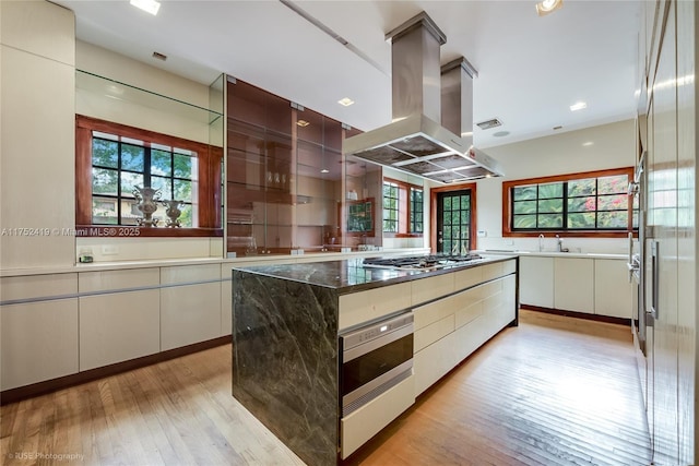 kitchen featuring island range hood, light wood-style flooring, modern cabinets, oven, and stainless steel gas cooktop