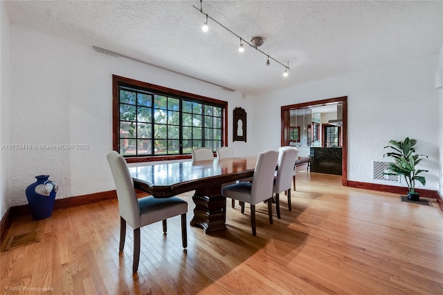 dining space with light wood-style floors, baseboards, and a textured ceiling