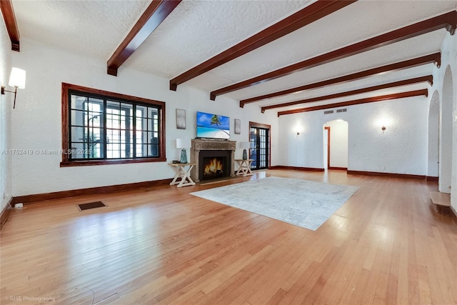 unfurnished living room with a textured ceiling, a warm lit fireplace, visible vents, light wood-style floors, and beam ceiling