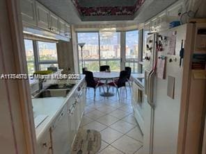 kitchen featuring light tile patterned floors, a tray ceiling, freestanding refrigerator, and a healthy amount of sunlight