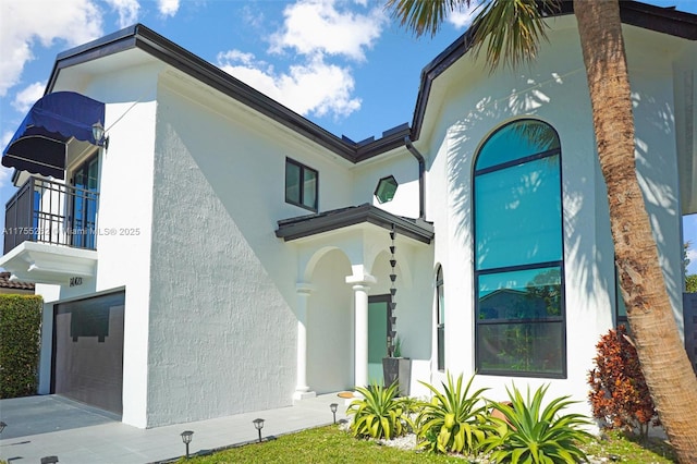 exterior space featuring an attached garage, a balcony, and stucco siding