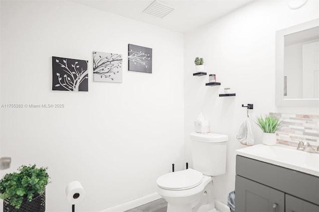 half bath featuring baseboards, visible vents, toilet, vanity, and backsplash