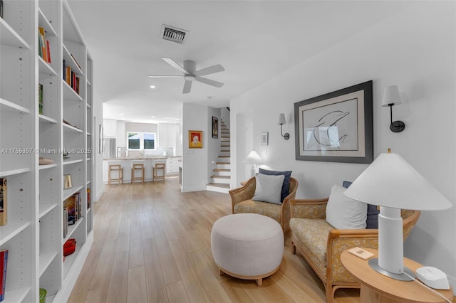 sitting room with light wood-style flooring, stairs, visible vents, and a ceiling fan