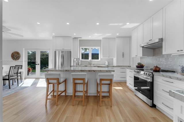 kitchen featuring under cabinet range hood, stainless steel appliances, a kitchen breakfast bar, french doors, and tasteful backsplash