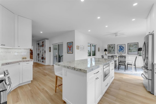 kitchen with light wood-style flooring, a kitchen island, appliances with stainless steel finishes, and decorative backsplash